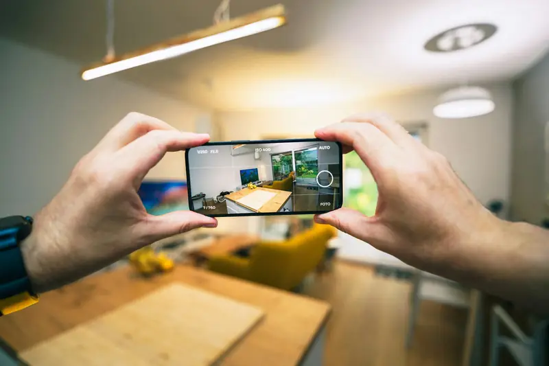 Manos tomando con el celular una foto de una sala y una cocina
