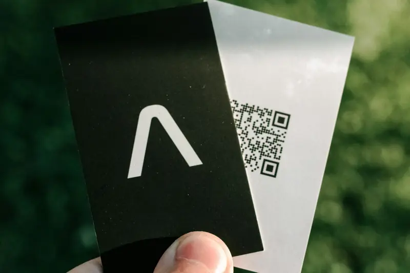 Mano sosteniendo dos tarjetas de presentación, una de ellas con un código QR